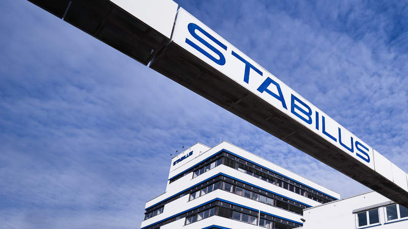 Firmengebäude der Stabilus Gruppe mit modernem Architekturdesign und einer markanten Brücke mit dem Schriftzug „STABILUS“ vor blauem Himmel.