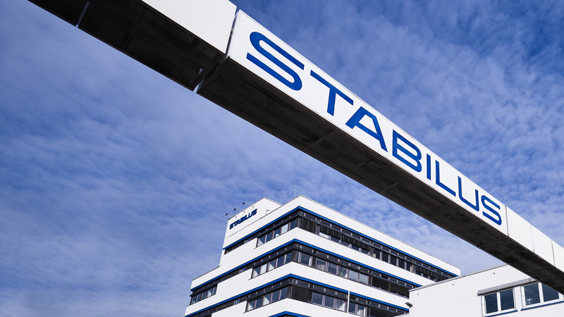 Firmengebäude der Stabilus Gruppe mit modernem Architekturdesign und einer markanten Brücke mit dem Schriftzug „STABILUS“ vor blauem Himmel.