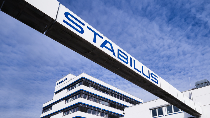 Firmengebäude der Stabilus Gruppe mit modernem Architekturdesign und einer markanten Brücke mit dem Schriftzug „STABILUS“ vor blauem Himmel.